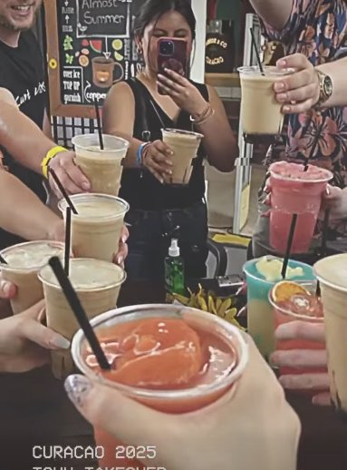 Still from the wrap-up video: fourteen people raising cocktails together around a bar table in Curacao